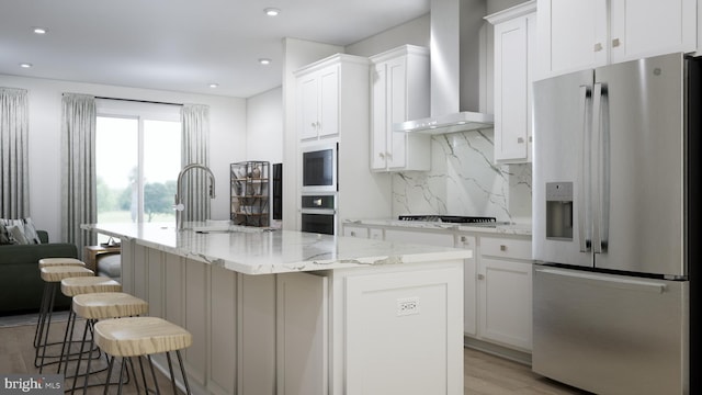 kitchen featuring white cabinets, a kitchen island with sink, wall chimney exhaust hood, appliances with stainless steel finishes, and a kitchen bar