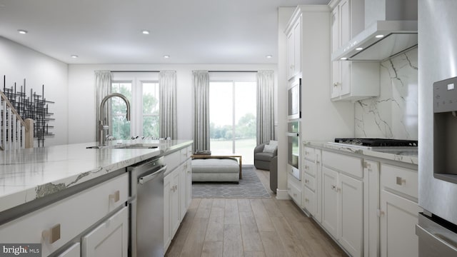 kitchen with light hardwood / wood-style floors, white cabinetry, wall chimney exhaust hood, light stone countertops, and stainless steel appliances