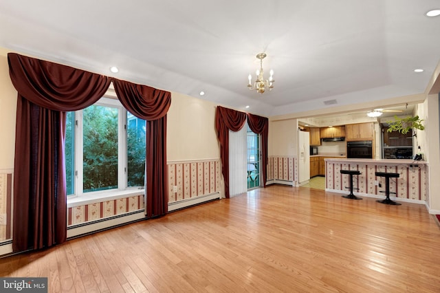 unfurnished living room with a notable chandelier, a raised ceiling, light hardwood / wood-style flooring, and baseboard heating