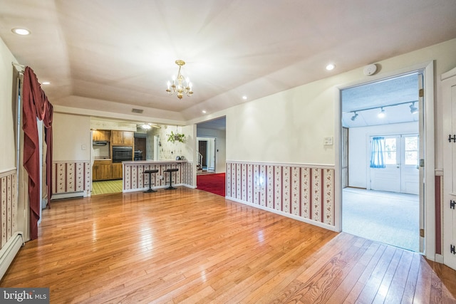 unfurnished living room featuring an inviting chandelier, light wood-type flooring, and a baseboard heating unit