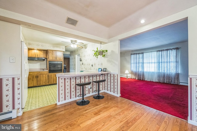 kitchen with oven, a kitchen bar, kitchen peninsula, light hardwood / wood-style floors, and white fridge