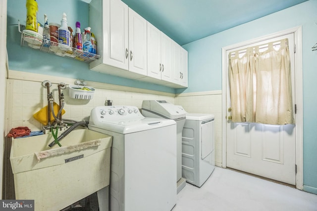 clothes washing area featuring tile walls, sink, washer and clothes dryer, and cabinets