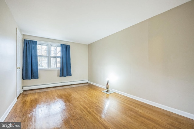 spare room featuring a baseboard heating unit and wood-type flooring