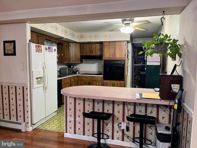 kitchen with kitchen peninsula, a breakfast bar area, black appliances, light hardwood / wood-style floors, and baseboard heating