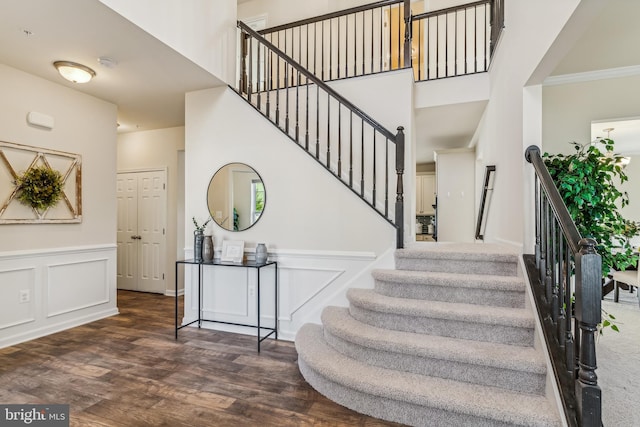 staircase featuring wood-type flooring, crown molding, and a high ceiling