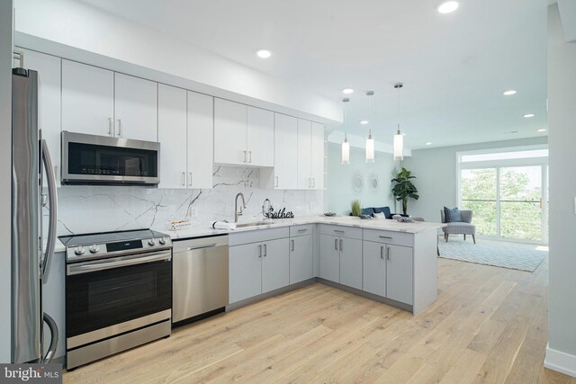 kitchen featuring hanging light fixtures, sink, kitchen peninsula, stainless steel appliances, and light hardwood / wood-style floors