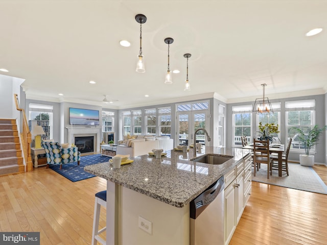 kitchen with light hardwood / wood-style floors, light stone countertops, decorative light fixtures, stainless steel dishwasher, and sink