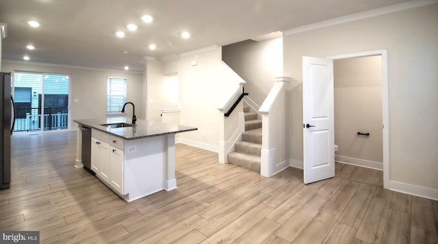 kitchen featuring white cabinets, dishwasher, dark stone countertops, a sink, and an island with sink