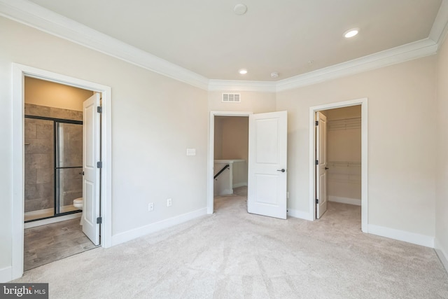 unfurnished bedroom featuring a closet, light colored carpet, connected bathroom, a walk in closet, and crown molding