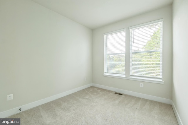 spare room with baseboards, visible vents, plenty of natural light, and light carpet