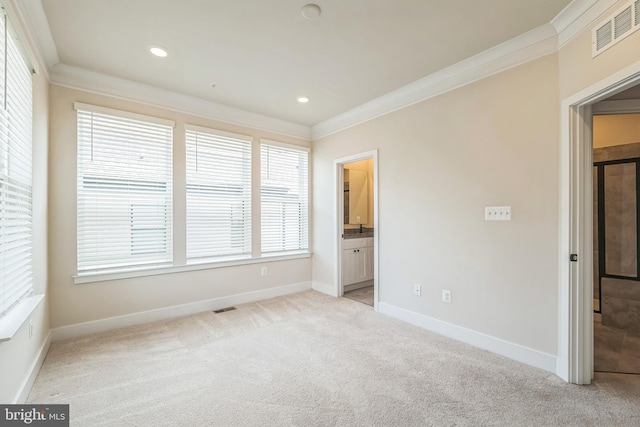 unfurnished bedroom with ensuite bath, multiple windows, light colored carpet, and crown molding