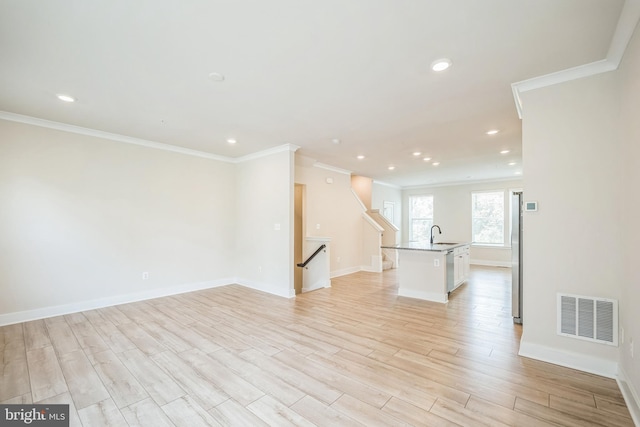 unfurnished living room featuring light wood finished floors, baseboards, visible vents, and ornamental molding