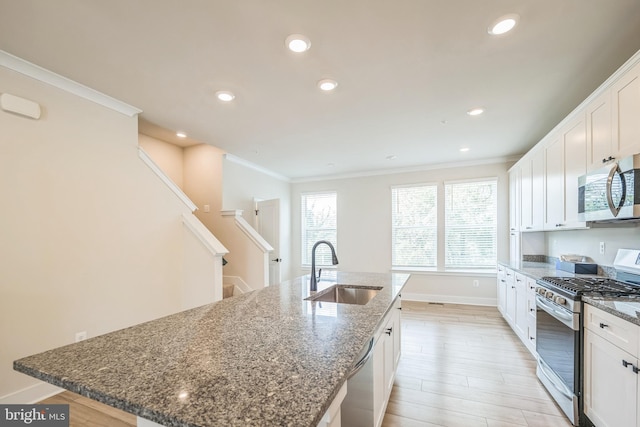 kitchen with white cabinets, sink, ornamental molding, a center island with sink, and appliances with stainless steel finishes