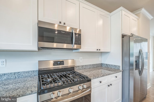 kitchen with light stone countertops, stainless steel appliances, white cabinetry, and light wood-type flooring