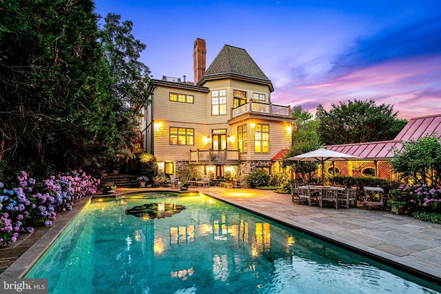 back house at dusk featuring a balcony and a patio