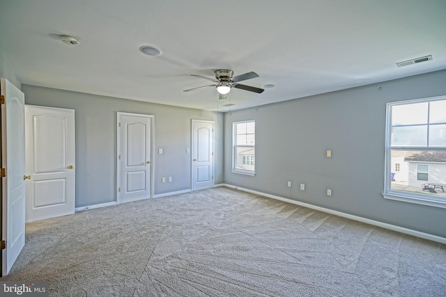 unfurnished bedroom with multiple windows, ceiling fan, two closets, and light colored carpet