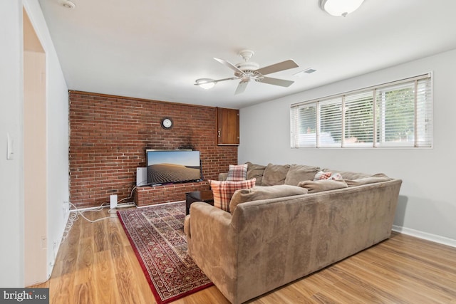 living room with ceiling fan, light hardwood / wood-style flooring, a brick fireplace, and brick wall