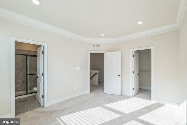 unfurnished bedroom with ornamental molding, a walk in closet, a closet, light colored carpet, and ensuite bath