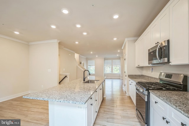 kitchen with an island with sink, stainless steel appliances, white cabinetry, and sink