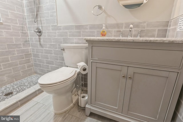 bathroom featuring tiled shower, vanity, toilet, and tile walls