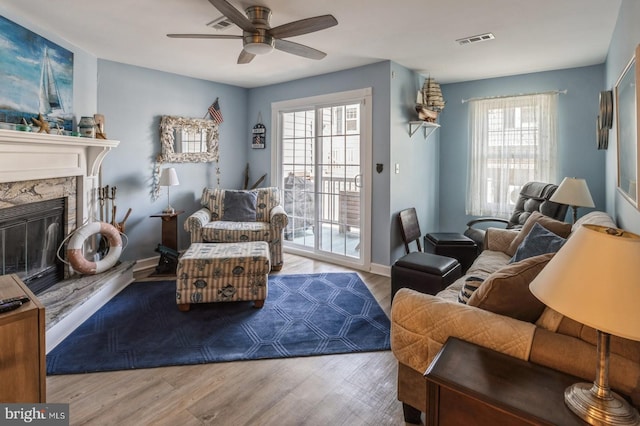 living room featuring ceiling fan, a stone fireplace, a wealth of natural light, and light hardwood / wood-style floors