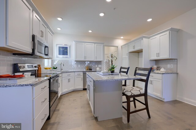 kitchen featuring appliances with stainless steel finishes, white cabinets, a breakfast bar area, a center island, and light hardwood / wood-style flooring