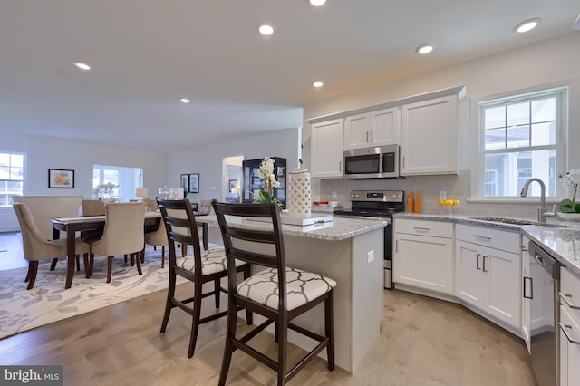 kitchen featuring light wood-type flooring, white cabinetry, light stone countertops, and stainless steel appliances