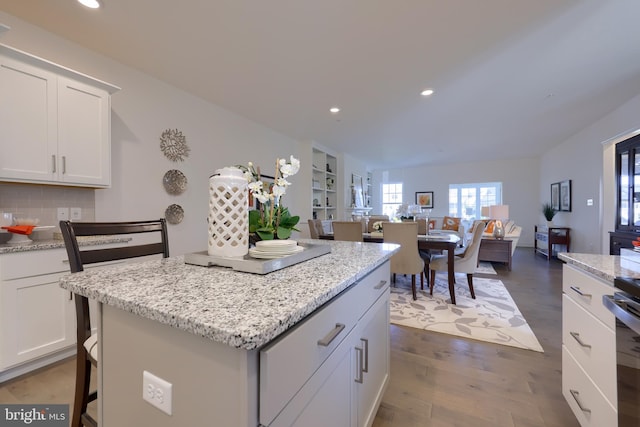 kitchen featuring a center island, dark hardwood / wood-style floors, a breakfast bar area, white cabinetry, and backsplash