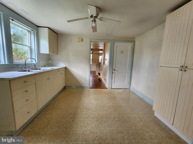 kitchen with ceiling fan, a textured ceiling, cream cabinets, and sink