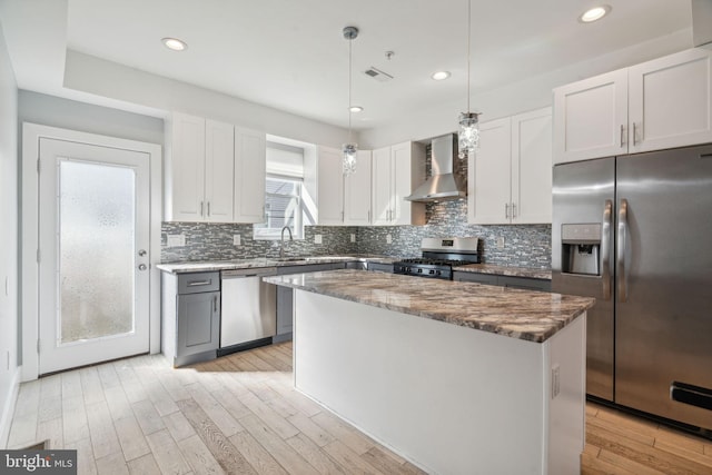 kitchen with wall chimney exhaust hood, pendant lighting, a kitchen island, white cabinets, and appliances with stainless steel finishes