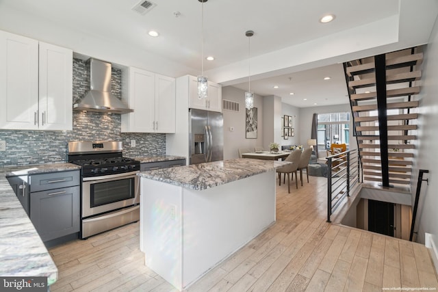 kitchen with wall chimney range hood, light hardwood / wood-style floors, light stone countertops, appliances with stainless steel finishes, and white cabinetry