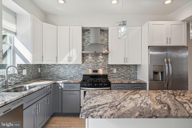 kitchen with stainless steel appliances, wall chimney range hood, white cabinets, and sink