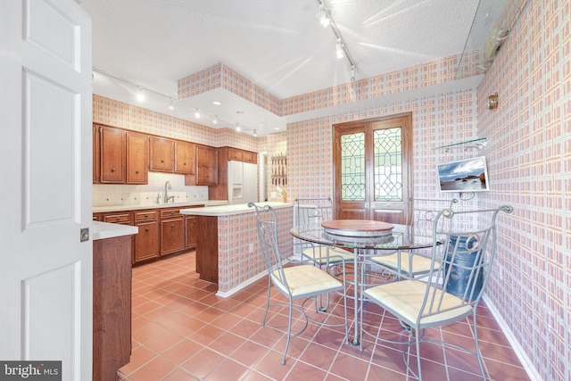 kitchen featuring sink, light tile patterned floors, white refrigerator with ice dispenser, track lighting, and a textured ceiling