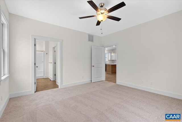 unfurnished bedroom with ceiling fan, light colored carpet, and ensuite bathroom