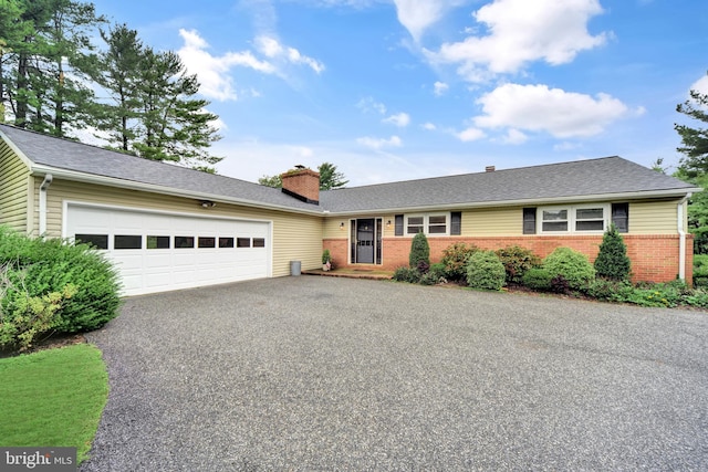 single story home featuring asphalt driveway, brick siding, a garage, a chimney, and roof with shingles