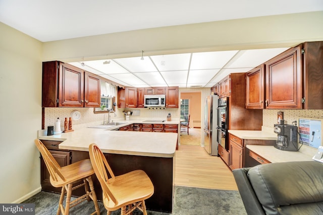 kitchen with appliances with stainless steel finishes, light countertops, a peninsula, and decorative backsplash