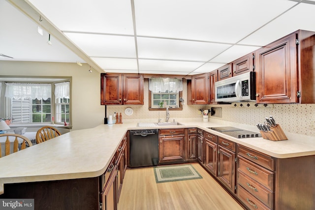 kitchen with black appliances, a sink, a peninsula, light wood-style floors, and light countertops