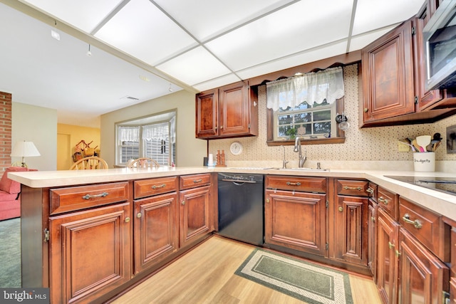 kitchen with a sink, black appliances, a peninsula, light wood-type flooring, and light countertops