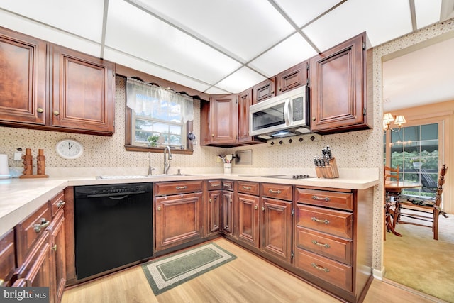 kitchen featuring black appliances, light countertops, a chandelier, and light wood-style floors