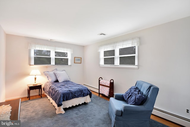 bedroom with a baseboard heating unit, wood finished floors, and baseboards