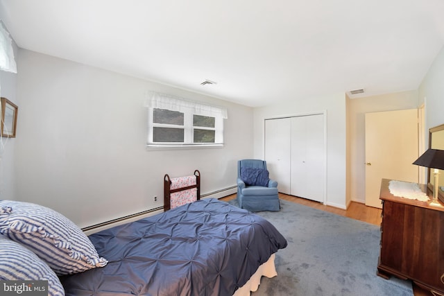 bedroom featuring a baseboard heating unit, wood finished floors, and a closet