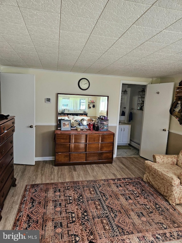 bedroom with wood finished floors, a baseboard radiator, and ensuite bath