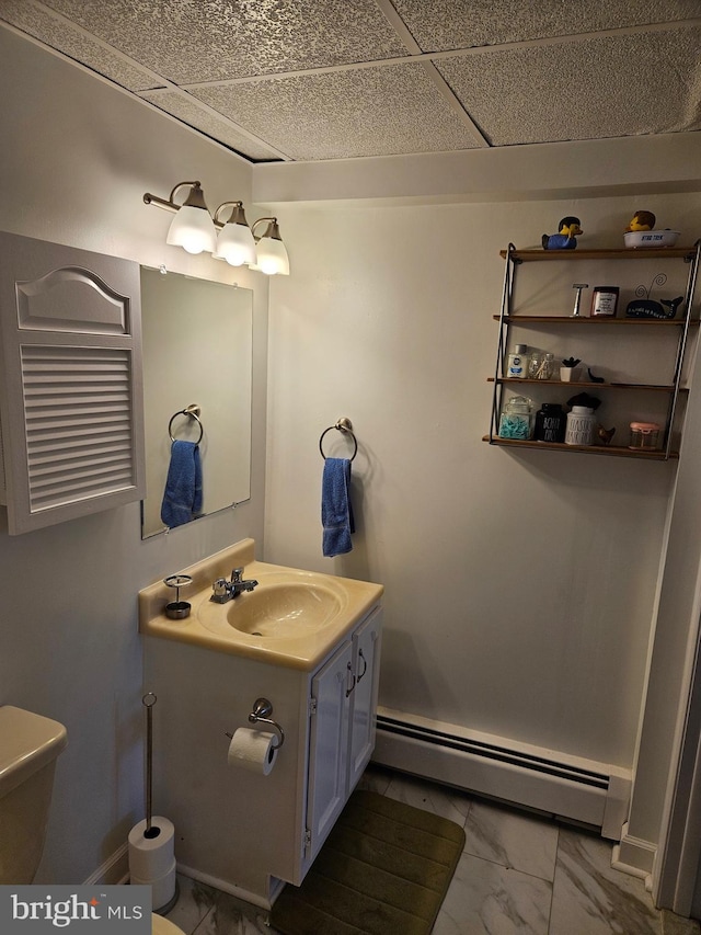 bathroom with a baseboard heating unit, marble look tile flooring, vanity, toilet, and baseboards