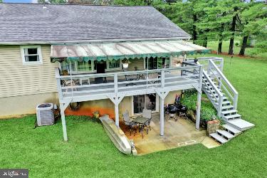 back of property with a wooden deck, central air condition unit, a patio, and a lawn