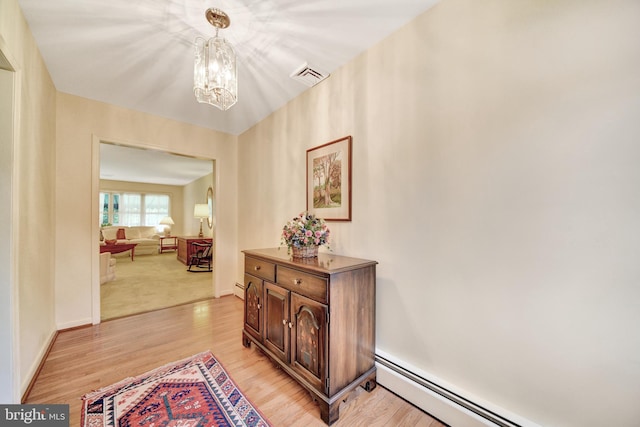 corridor with a chandelier, a baseboard radiator, light wood finished floors, and baseboard heating