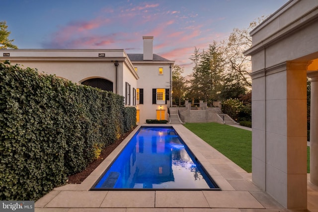 pool at dusk featuring a lawn