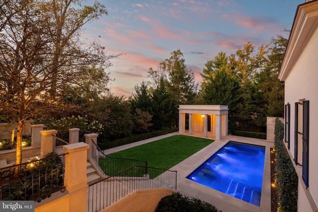 pool at dusk featuring a lawn