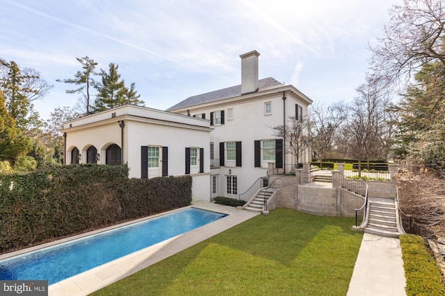 rear view of house with a fenced in pool and a lawn