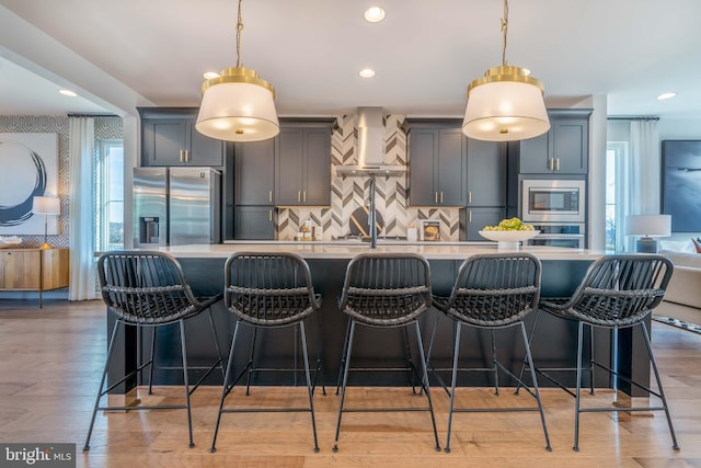 kitchen featuring decorative light fixtures, appliances with stainless steel finishes, wall chimney range hood, and a breakfast bar