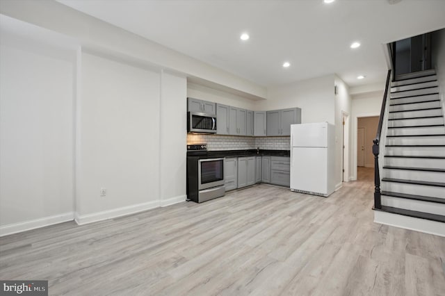 kitchen with appliances with stainless steel finishes, gray cabinetry, light hardwood / wood-style floors, and decorative backsplash